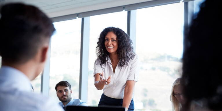 Businesswoman Stands To Address Meeting Around Board Table